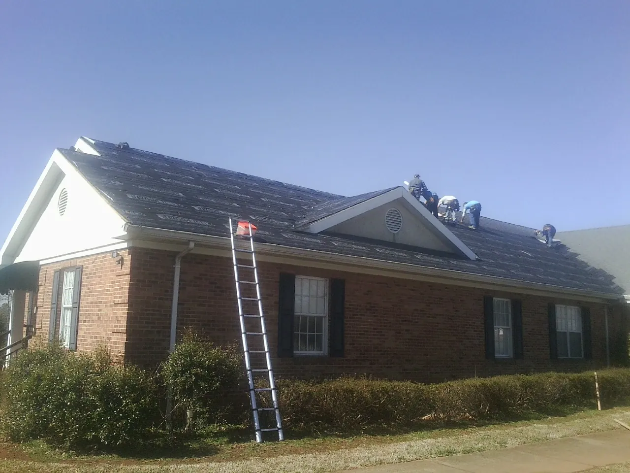 Crew tearing shingles off a brick ranch roof with a ladder set — Metal Roof Repair work by our crew in Burlington